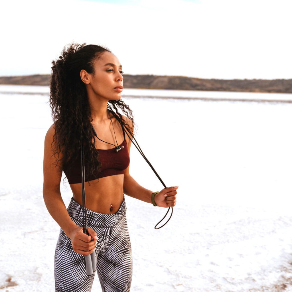 African American woman on the beach with a jump rope on her shoulders 